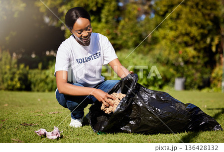 Volunteer, woman and cleaning waste in park for community service, pollution and climate change or earth day project. African person volunteering in garden, nature or outdoor and plastic bag or trash 136428132