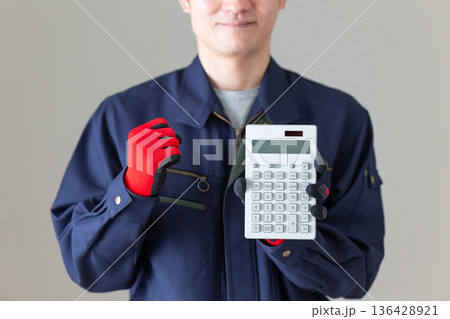 電卓を持ってガッツポーズする作業服のミドル男性ビジネスマン 136428921