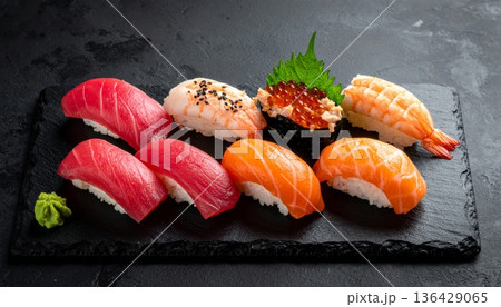 Gourmet salmon and tuna maki sushi with chopsticks on a black plate featuring fresh ginger and wasabi for a healthy Japanese seafood meal 136429065