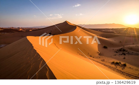 An orange sun sets over the red sand dunes of the Sahara, creating a hot wilderness landscape during a dry summer adventure in the arid Morocco desert 136429619