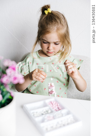 Young girl sorting colorful candies on a table with flowers nearby Young girl sorting colorful candies on a table with flowers nearby 136430881