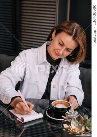 Woman writing notes in cafe while enjoying coffee on a sunny day Woman writing notes in cafe while enjoying coffee on a sunny day 136430900