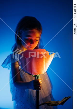 Young child interacts with oversized flower in soft blue light during creative activity 136430911