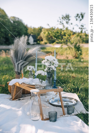 Elegant outdoor picnic setup with flowers and decorative elements in a serene setting Elegant outdoor picnic setup with flowers and decorative elements in a serene setting 136430915