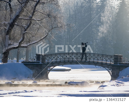 A man is taking a picture of a bridge over a frozen river 136431527