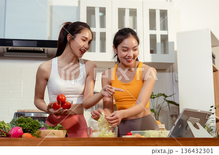 Two sporty women drinking green smoothie and eating fresh vegetables. 136432301