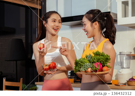 Two sporty women drinking green smoothie and eating fresh vegetables. 136432312