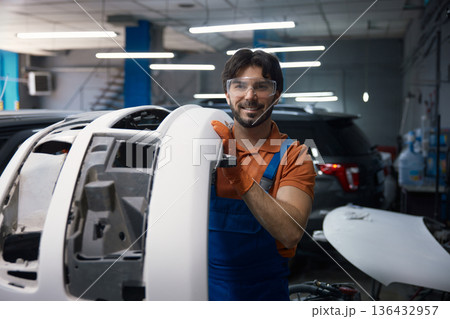 Smiling automotive technician holding car bumper in garage 136432957