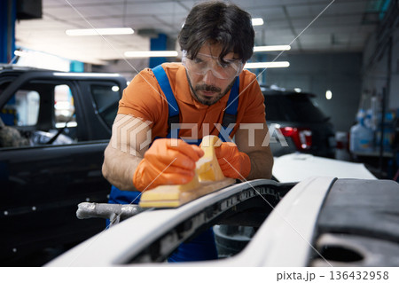 A mechanic is sanding a car bumper in an automotive garage specializing in bodywork A mechanic is sanding a car bumper in an automotive garage specializing in bodywork 136432958