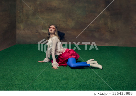 Young woman in colorful outfit lying on green studio floor smiling dreamily upward. Young woman in colorful outfit lying on green studio floor smiling dreamily upward. 136433999