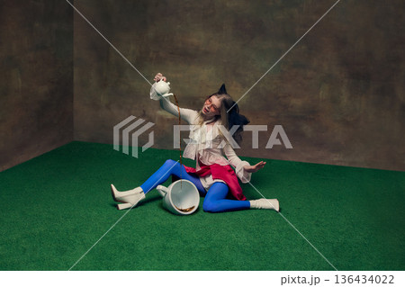 Woman pouring tea into oversized cup in whimsical studio setting. 136434022