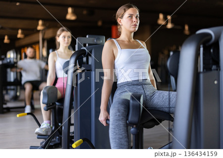 Slender athletic girl work out muscles of legs and thighs on simulator in fitness club 136434159