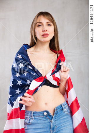 Flirting young woman with American flag against gray wall indoors 136434171
