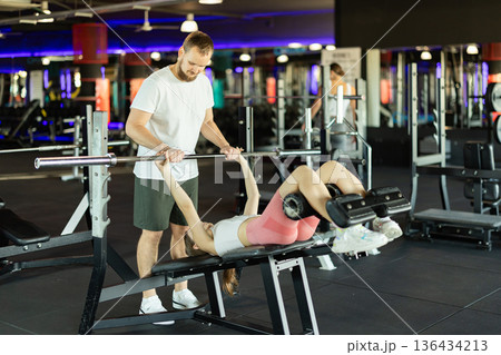 Young man trainer trains woman with barbell Young man trainer trains woman with barbell 136434213