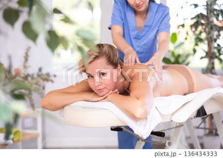 Woman relaxing while professional masseuse doing back massage Woman relaxing while professional masseuse doing back massage 136434333