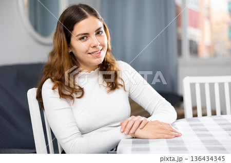 Smiling woman sitting at table at home Smiling woman sitting at table at home 136434345