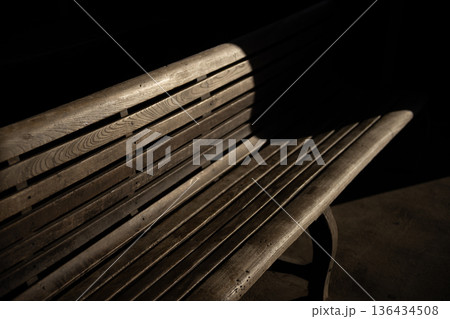 暗闇に差し込む一筋の光と木製ベンチ 静寂な空間に浮かび上がる孤独と休息のイメージ 136434508