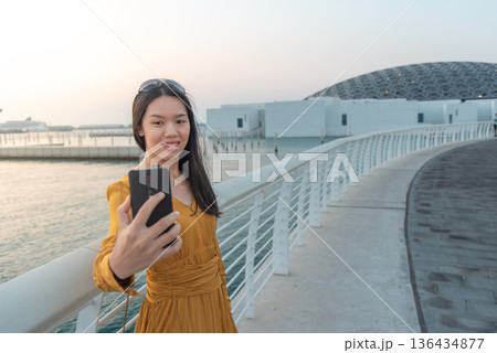 Fashionable Young Asian Woman Taking Selfie Outside museum area in Abu Dhabi United Arab Emirates 136434877