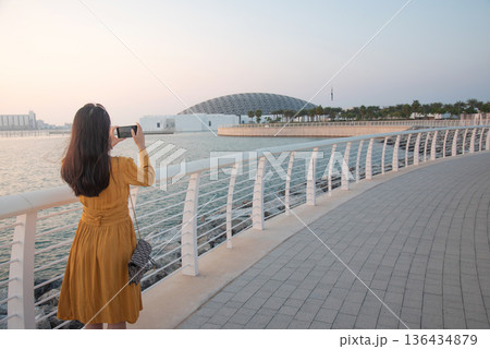 Rear View of Fashionable Young Woman Taking Photo Outside Louvre Abu Dhabi at Sunset Rear View of Fashionable Young Woman Taking Photo Outside Louvre Abu Dhabi at Sunset 136434879