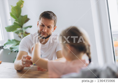 Father and daughter play with a puzzle cube at home, sitting at a wooden table and enjoying mindful time together 136435066