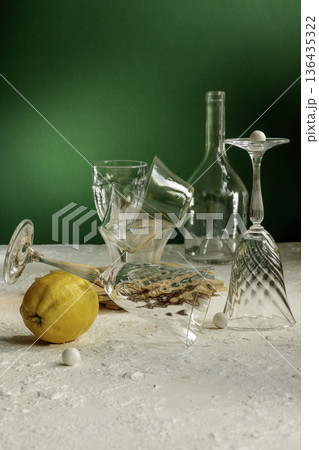 Dramatic still life with broken crystal wine glass, scattered salt and lemon on white table. Dramatic still life with broken crystal wine glass, scattered salt and lemon on white table. 136435322