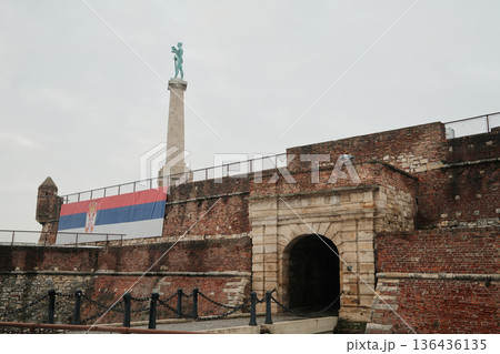 Kalemegdan Fortress entrance with Serbian flag and Victory Monument above, showing historic walls, winter atmosphere and national symbolism in Belgrade 136436135