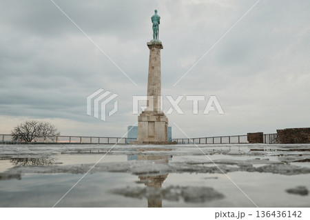 Victory Monument in Kalemegdan Fortress reflected in wet stone surface after snow, creating dramatic symmetry and minimalist winter city landmark composition 136436142