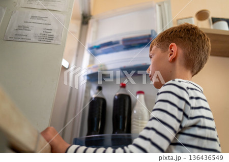 Young boy looking into open refrigerator at home, everyday domestic lifestyle 136436549
