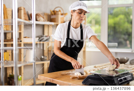 Elderly woman cuts and weighs pieces of dough 136437896