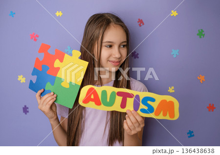 A child holds the inscription autism and bright multicolor puzzle, symbolizing Awareness Day about autism. Specialized school for children with autism. Purple background with puzzle pieces A child holds the inscription autism and bright multicolor puzzle, symbolizing Awareness Day about autism. Specialized school for children with autism. Purple background with puzzle pieces 136438638