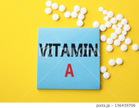 Vitamin A symbol. Concept word Vitamin A on blue note. Beautiful yellow background with pills. Medicine and Vitamin A concept. Copy space Vitamin A symbol. Concept word Vitamin A on blue note. Beautiful yellow background with pills. Medicine and Vitamin A concept. Copy space 136439706