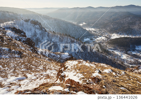 Panoramic view of snow capped mountains, forest landscape with village in valley. Winter season natural beauty and serenity. Arch rock, Torgashinsky ridge, Krasnoyarsk, Siberia 136441026