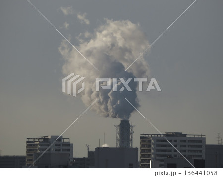 冬の空に立ち上る工場の白い煙と都市のビル群の風景 136441058