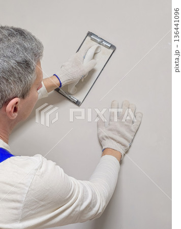 Vertical view the hand of a worker and a tool for grinding putty. Vertical view the hand of a worker and a tool for grinding putty. 136441096