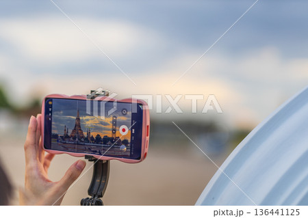 Tourists take photos with their smartphones at Wat Arun Ratchawararam Ratchaworamahawihan during sunset in Bangkok, Thailand. 136441125
