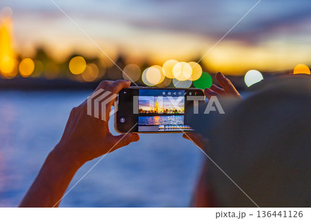 Tourists take photos with their smartphones at Wat Arun Ratchawararam Ratchaworamahawihan during sunset in Bangkok, Thailand. 136441126
