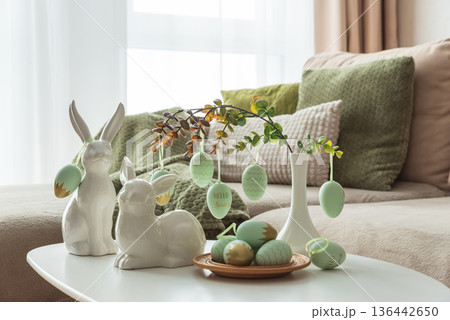 Cozy Easter Living Room Decor with Bunny Figurines and Hanging Eggs on White Table 136442650