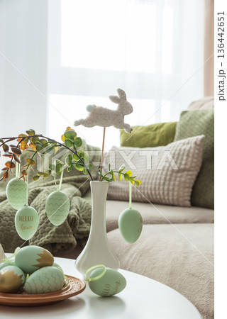 Cozy Easter Living Room Decor with Bunny Figurines and Hanging Eggs on White Table 136442651