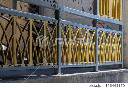 a bright yellow lattice of arched bars cuts a striking silhouette against a muted, weathered backdrop. Anchored by a heavy gray frame, the railing balances decorative flair with structural grit. a bright yellow lattice of arched bars cuts a striking silhouette against a muted, weathered backdrop. Anchored by a heavy gray frame, the railing balances decorative flair with structural grit. 136443170