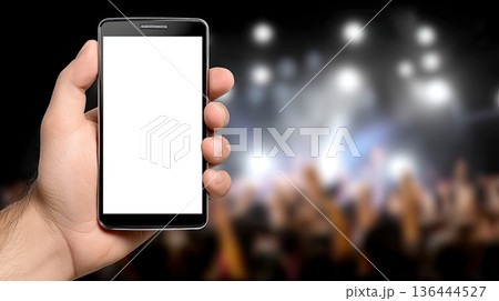 A hand holds a mobile phone displaying a blank screen while people are seen dancing in a night club environment and bright lights A hand holds a mobile phone displaying a blank screen while people are seen dancing in a night club environment and bright lights 136444527