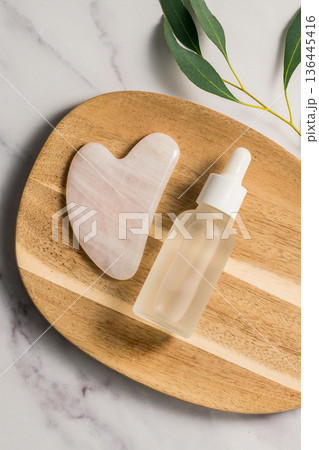 Rose quartz gua sha tool and oil bottle on wooden tray, face massage tool, beauty abstract photo. Copy space 136445416