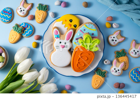 Easter holiday background with easter cookies in a plate: bunny, chick, carrot and egg on blue background, with mini chocolate egg candies Easter holiday background with easter cookies in a plate: bunny, chick, carrot and egg on blue background, with mini chocolate egg candies 136445417