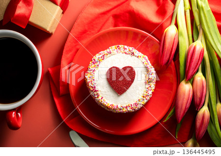 Valentine's Day festive red background. Cake with red heart, cup of coffee, gift box and spring red tulip flower bouquet. Top view Valentine's Day festive red background. Cake with red heart, cup of coffee, gift box and spring red tulip flower bouquet. Top view 136445495