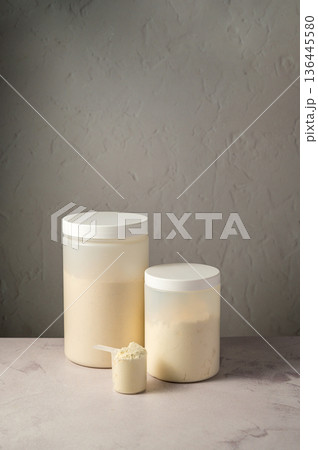 Protein powder in scoop with white plastic protein tubes, jars in background. Body building, muscle growth and food supplement concept Protein powder in scoop with white plastic protein tubes, jars in background. Body building, muscle growth and food supplement concept 136445580