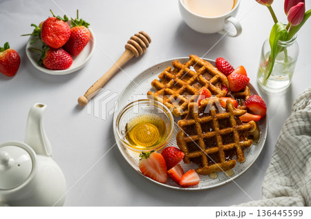 Belgian waffles with strawberries and honey, cup of tea and fresh fruits. Homemade breakfast table setting with tulip flower bouquet 136445599