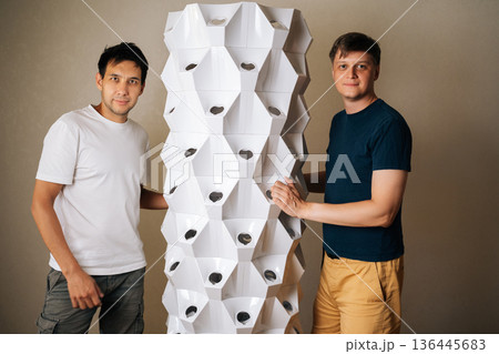 Portrait of male gardeners presenting vertical hydroponic tower, showcasing innovative urban farming technology supporting local sustainable agriculture and environmentally friendly growing methods. 136445683