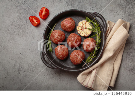 Raw meatballs with garlic and rosemary in cast iron pan on gray concrete background, copy space 136445910