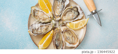 Fresh oysters with lemon wedges and oyster knife on plate top view Fresh oysters with lemon wedges and oyster knife on plate top view 136445922