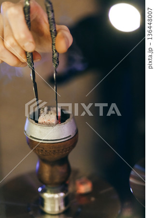 Hand Placing Charcoal On Hookah Bowl In Dimly Lit Lounge Hand Placing Charcoal On Hookah Bowl In Dimly Lit Lounge 136448007