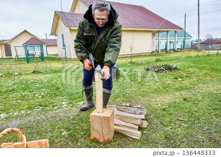 Preparation for heating season in household with stove heating, homeowner splits logs into thin chips to create kindling material. Preparation for heating season in household with stove heating, homeowner splits logs into thin chips to create kindling material. 136448333